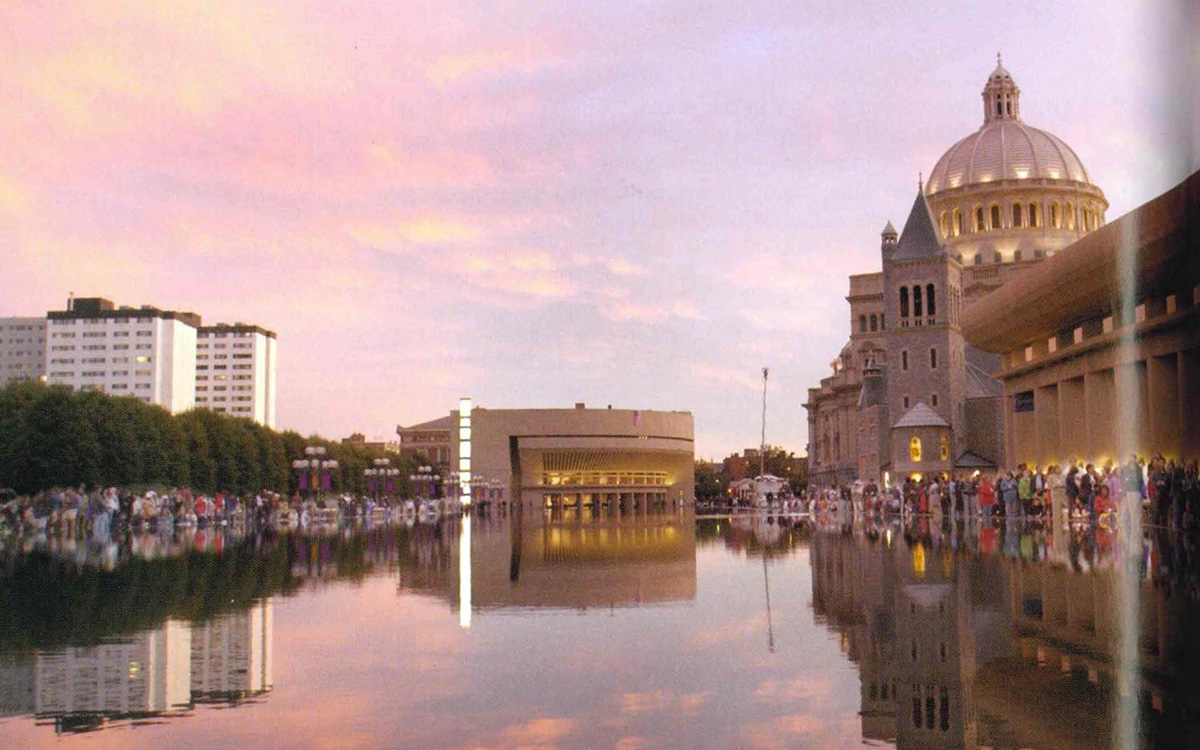 Image description: A wide view of the reflecting pool on the Christian Science Plaza at dusk, the sky pink with the sunset. Hundreds of people line the reflecting pool. The Mother Church is visible in the top right of the photo.