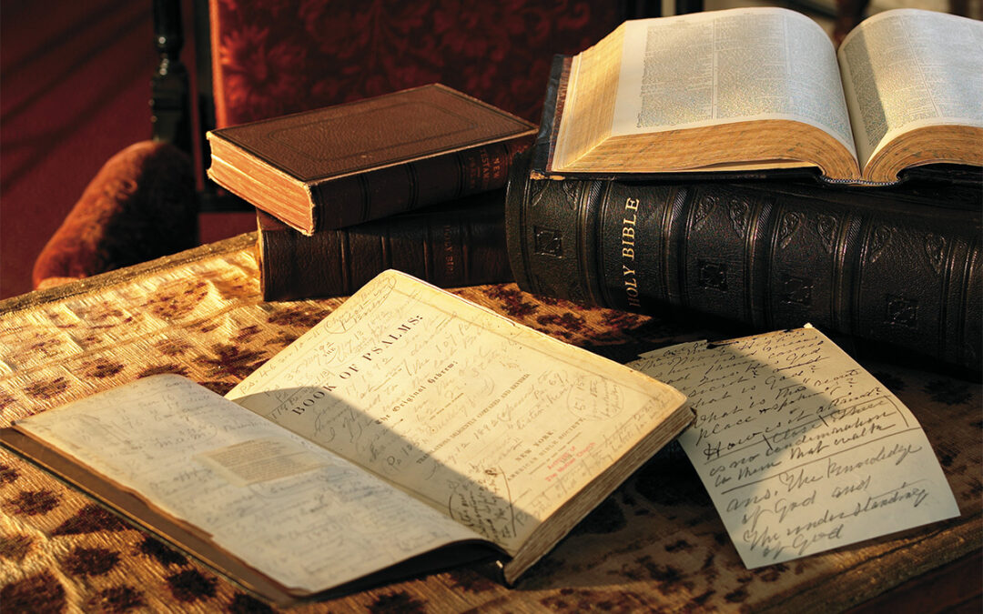 Table with multiple books on top. Bible is open to Book of Psalms with many handwritten notes on the page