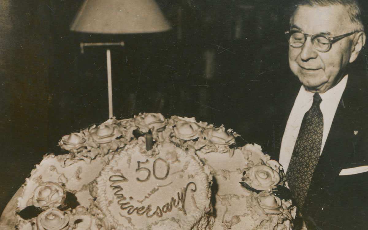 Paul Deland posing with a decorated cake that says, "50th Anniversary"