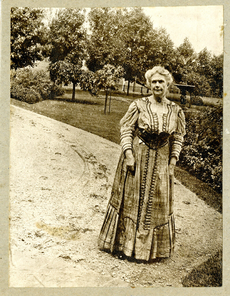 Sarah Jane Clark outisde. Standing on a road or path, with trees in the background. 