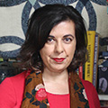 Headshot of Laura Prieto, in red shirt with books in the background