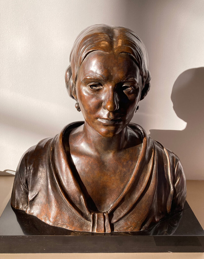 A copper-colored bust of Dorothy Adlow sits mounted on a flat countertop.